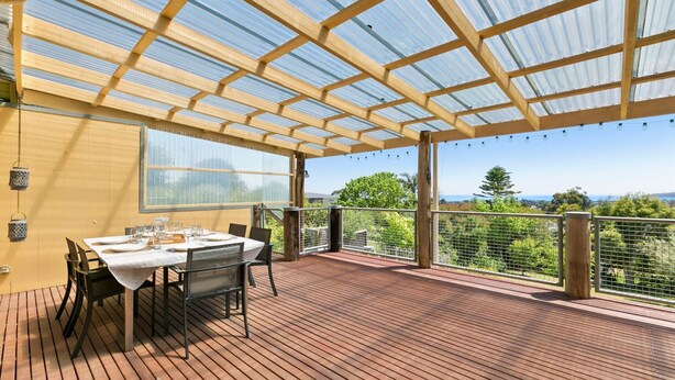 Uma área de refeições ao ar livre coberta, com uma mesa posta para quatro pessoas, com vista para uma paisagem deslumbrante.