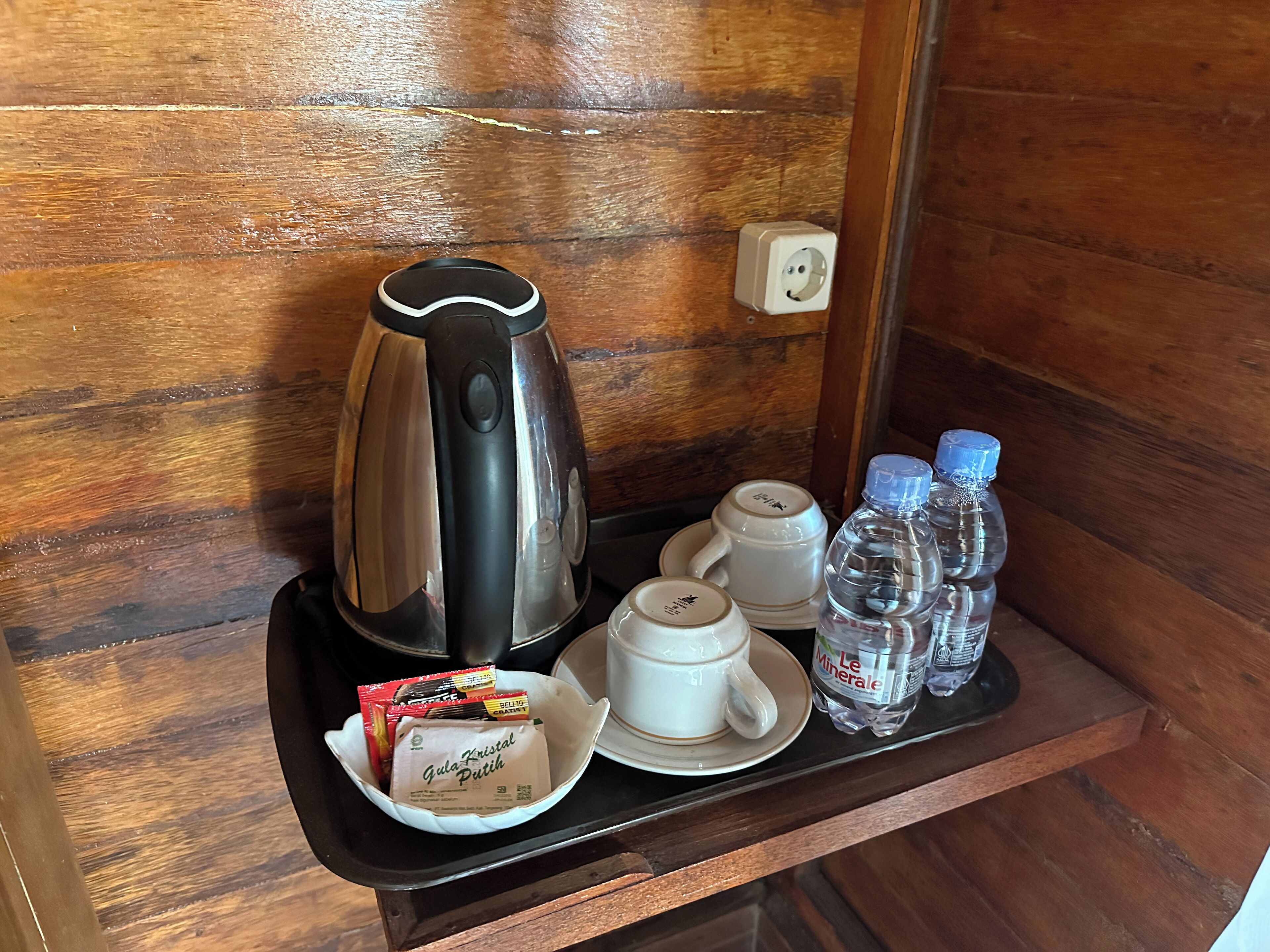 A tray with a coffee maker, two cups, a plate with a bag of snacks, and two water bottles.