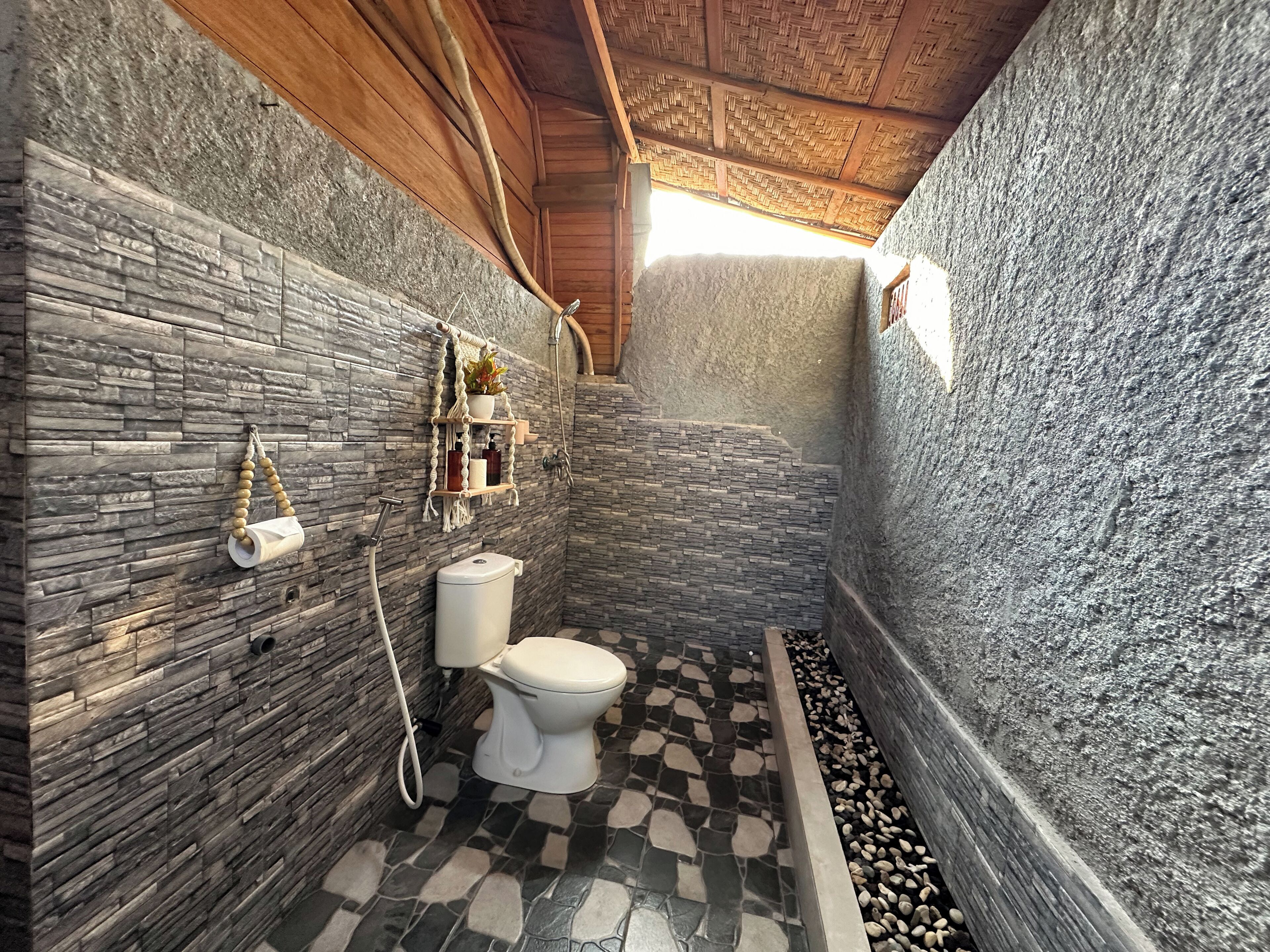 A bathroom with stone walls, a toilet, a shower, and a small shelf with toiletries.