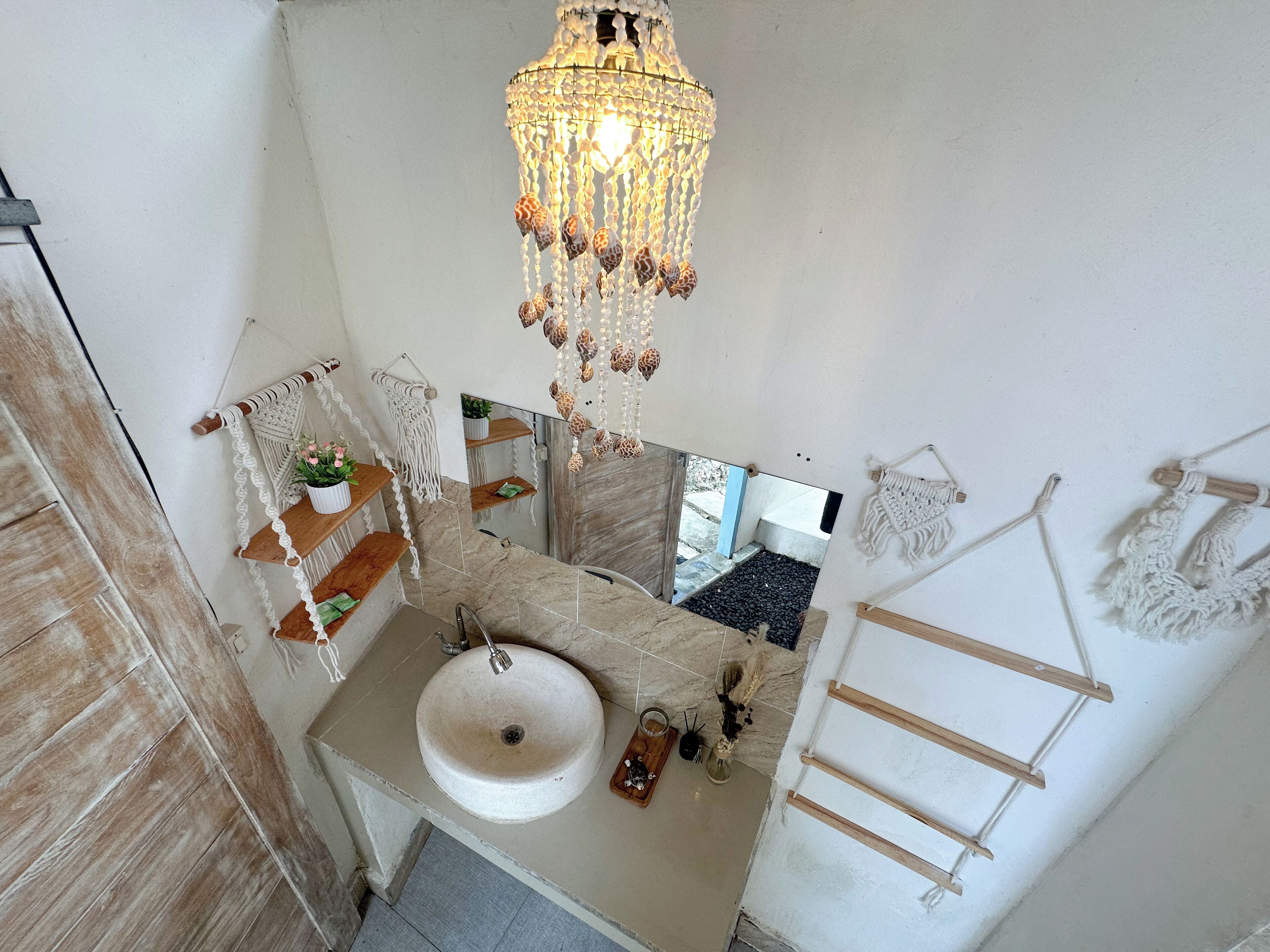A bathroom with a white sink, wooden shelves, a mirror, and a macramé towel rack.