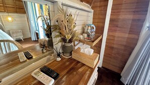 A wooden interior with a wooden desk, two potted plants, a tray with a kettle, cups, and a bottle. There are two remote controls and a white device on the desk. - Sunset Hill Penida Resort (Penida Island)