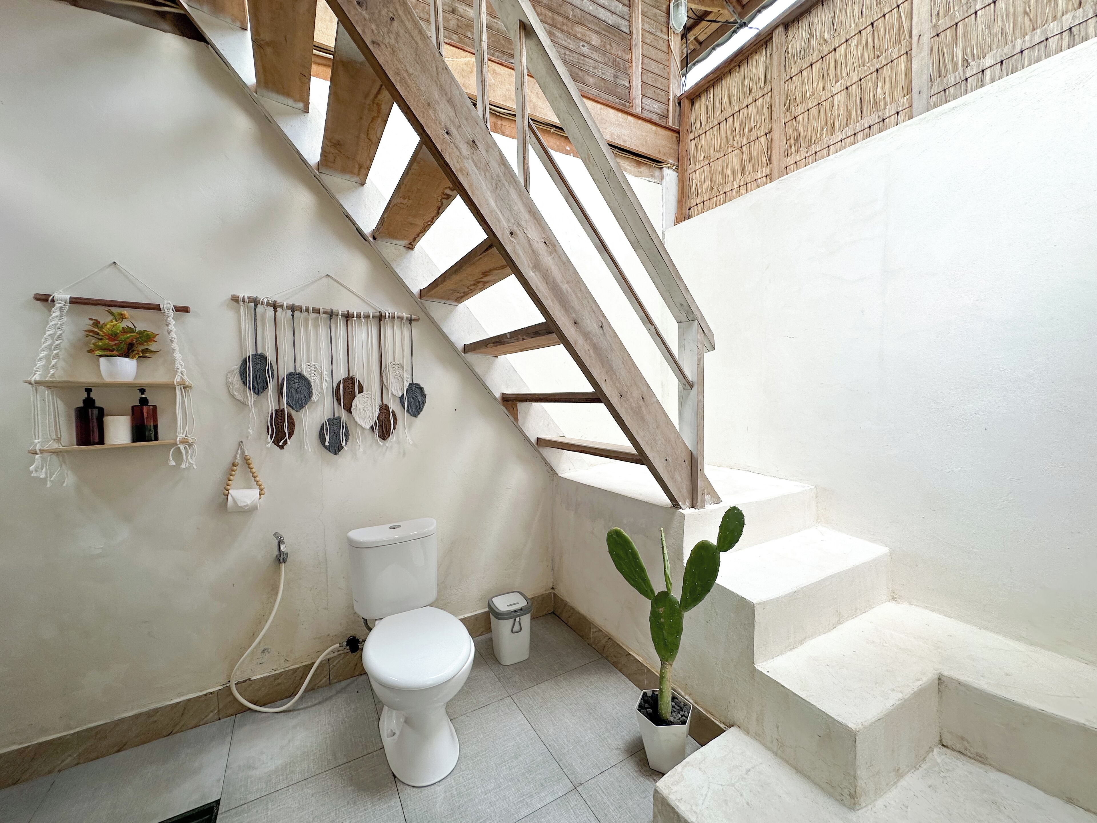 A bathroom with a white toilet, a sink, a shower, and a staircase leading to an upper level.