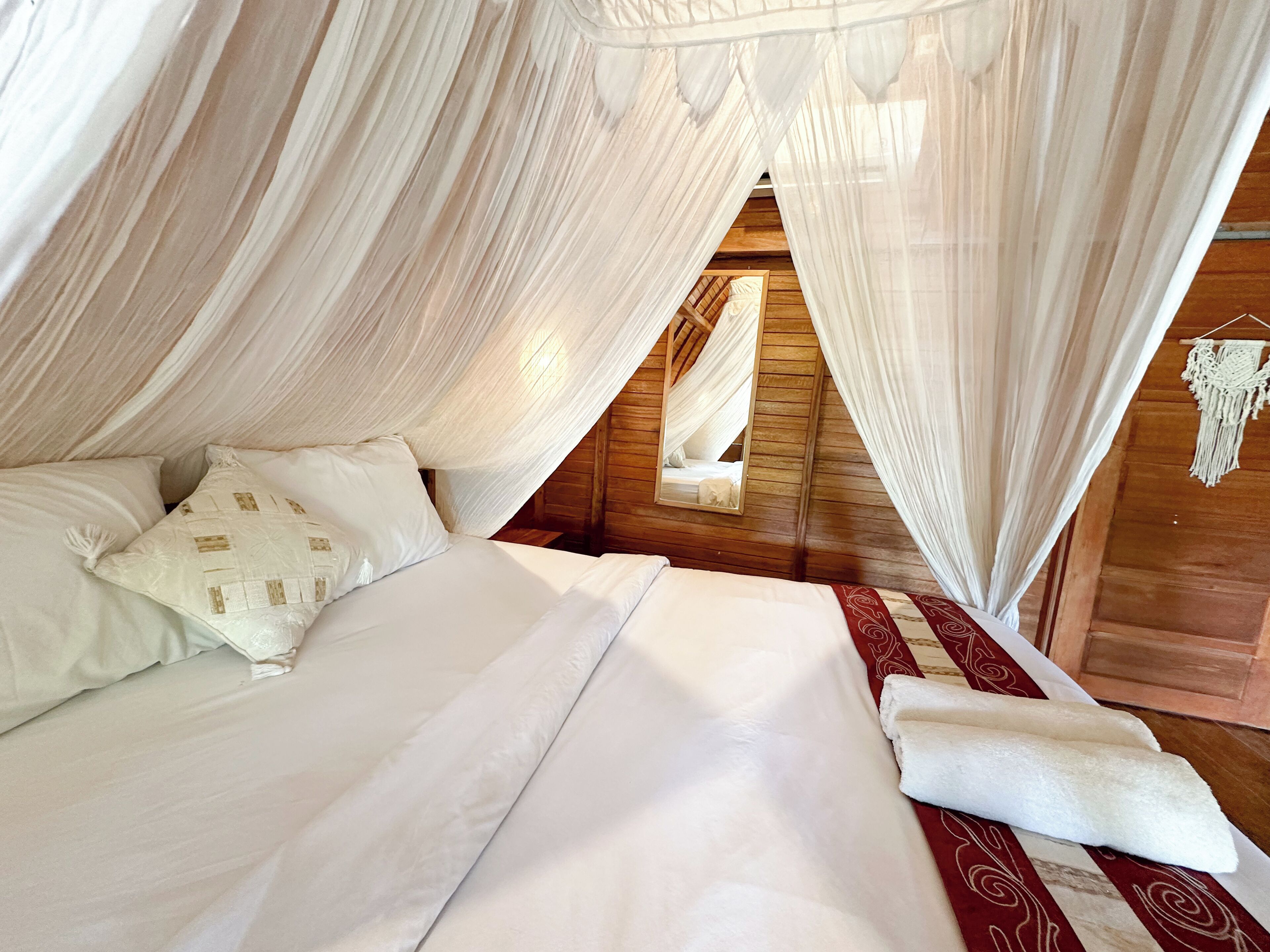Ein Bett mit weißen Bettwäsche und einer roten, gemusterten Tagesdecke, drapiert mit weißen Vorhängen.