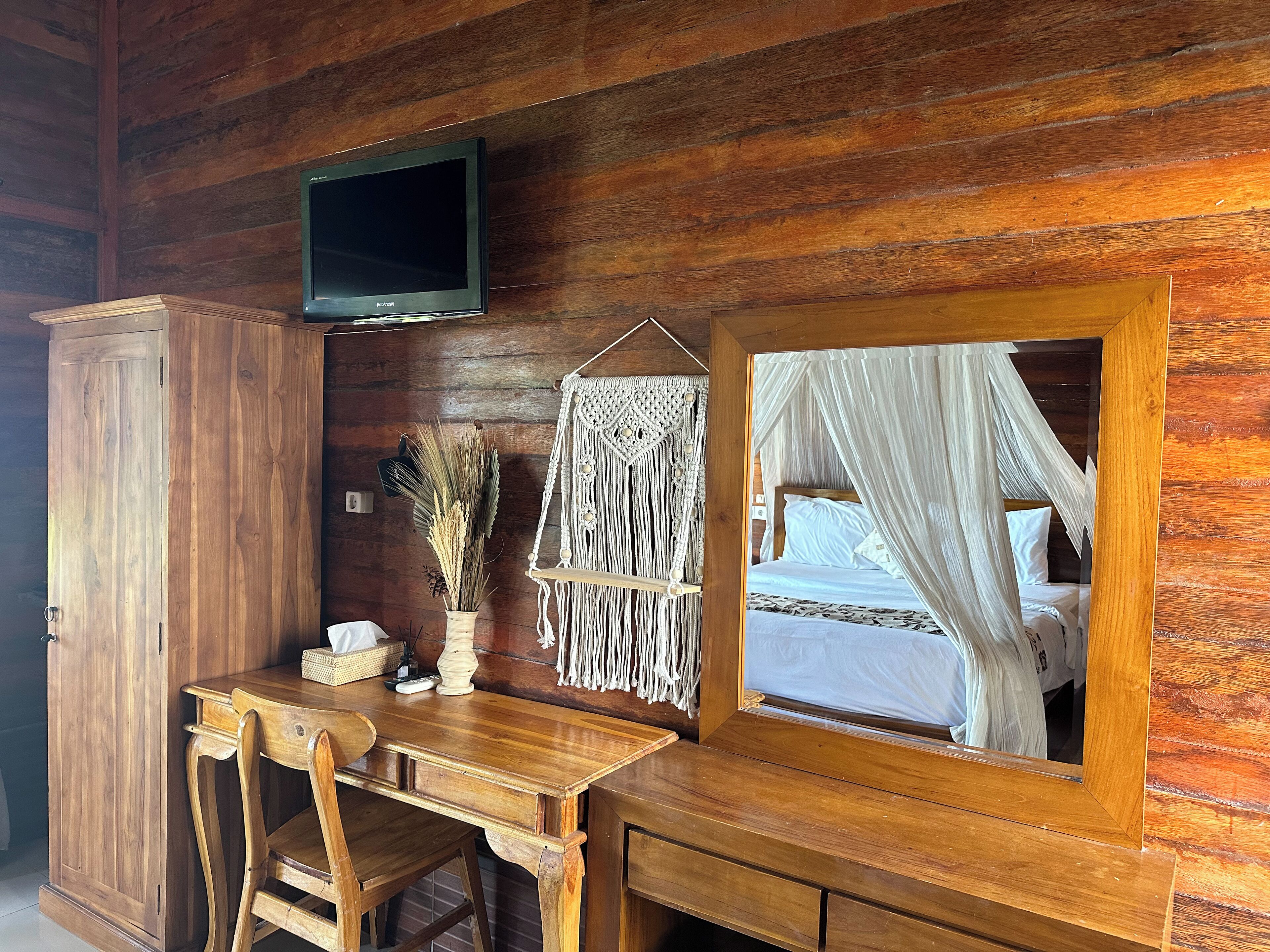 A wooden cabin room with a bed, a TV, a desk, and a mirror.