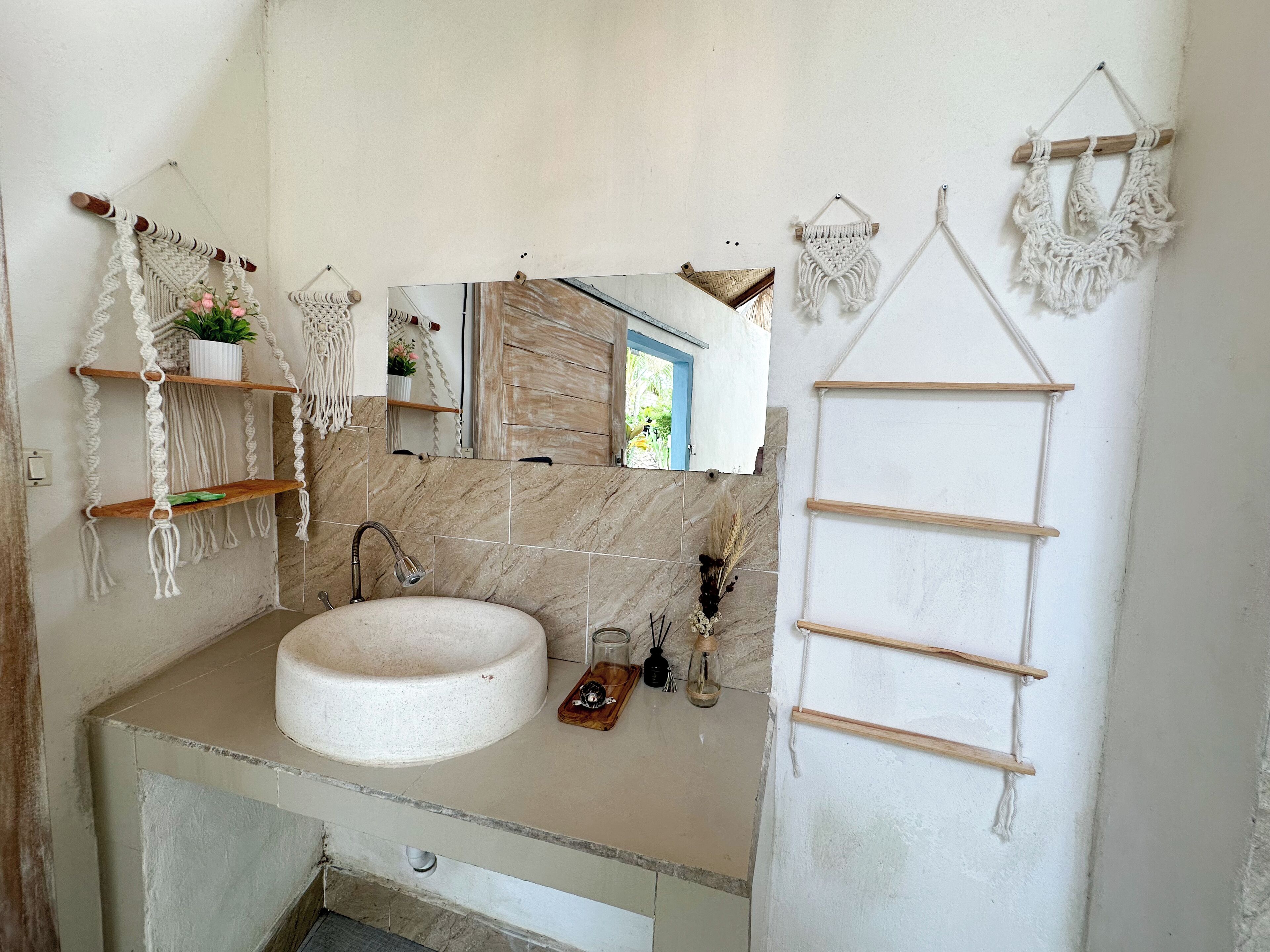 A bathroom with a round sink, a mirror, and macramé wall decorations.