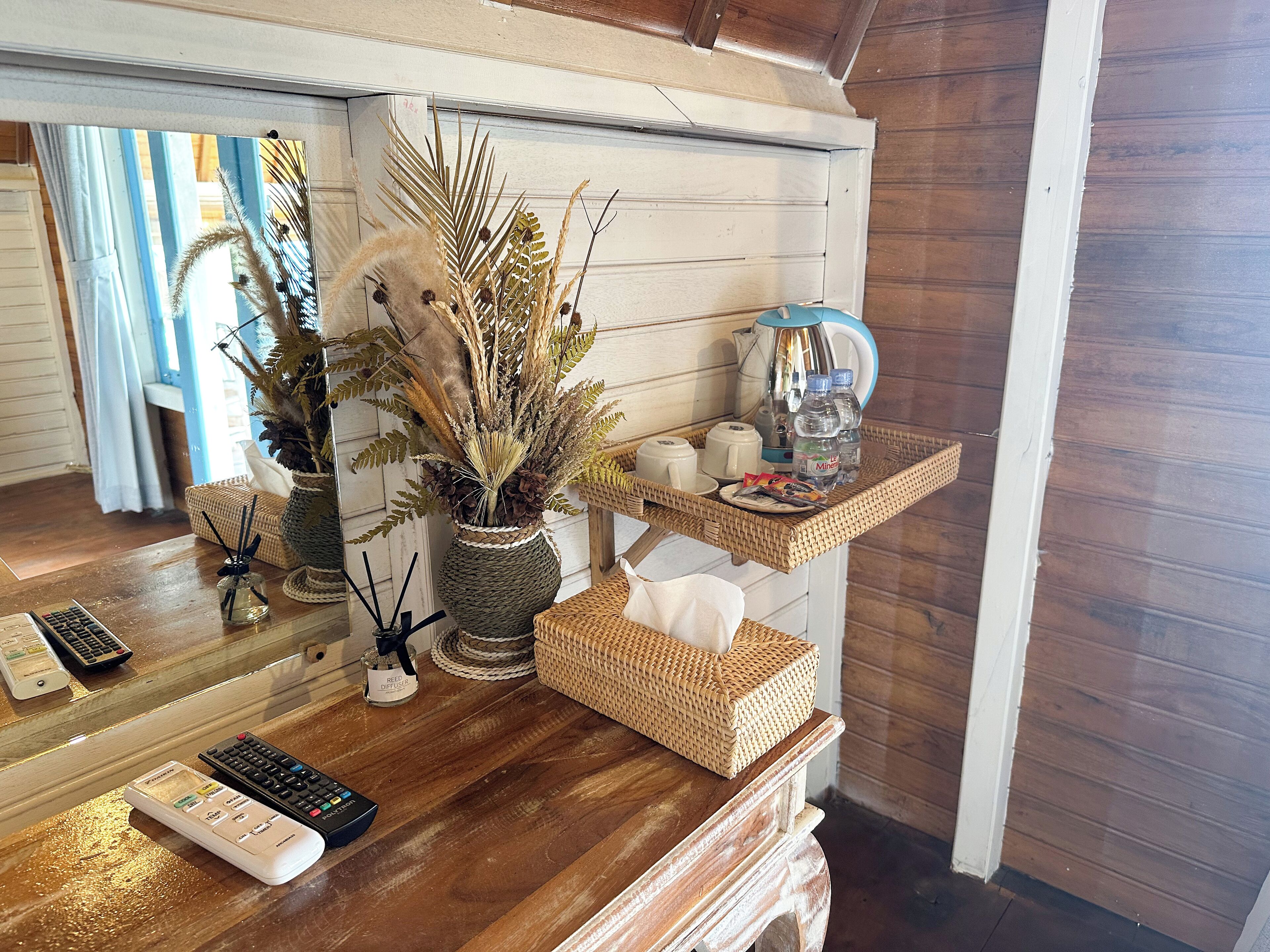 A wooden reception desk with a woven basket, a vase with dried plants, a coffee maker, and a water bottle.