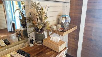 A wooden reception desk with a woven basket, a vase with dried plants, a coffee maker, and a water bottle.