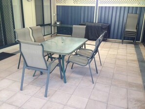 Une terrasse extérieure avec une table à plateau en verre et quatre chaises.