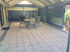 Une terrasse couverte avec une table et des chaises, une vue sur le jardin par une porte vitrée et un plafond avec des poutres en bois.