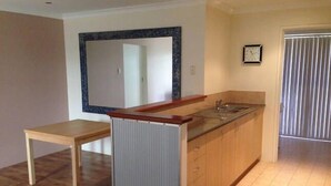 A kitchen with a wooden countertop, a sink, and a mirror above it. There is a wooden table and a door leading to another room.