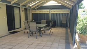 An outdoor patio with a table and chairs, a covered area with a ceiling, and a potted plant.