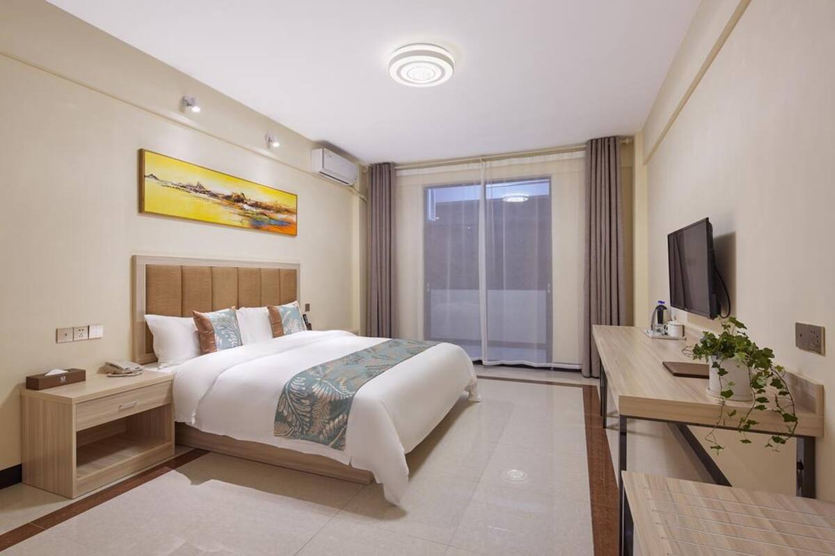 Una camera d'albergo con un letto grande, una scrivania con televisione, un quadro appeso e una finestra con tende.