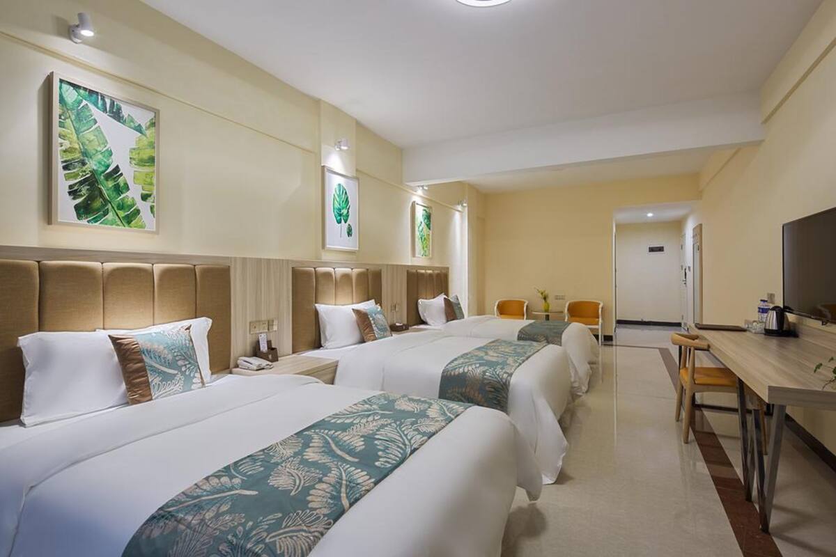 Camera d'albergo con tre letti, una scrivania e una televisione.