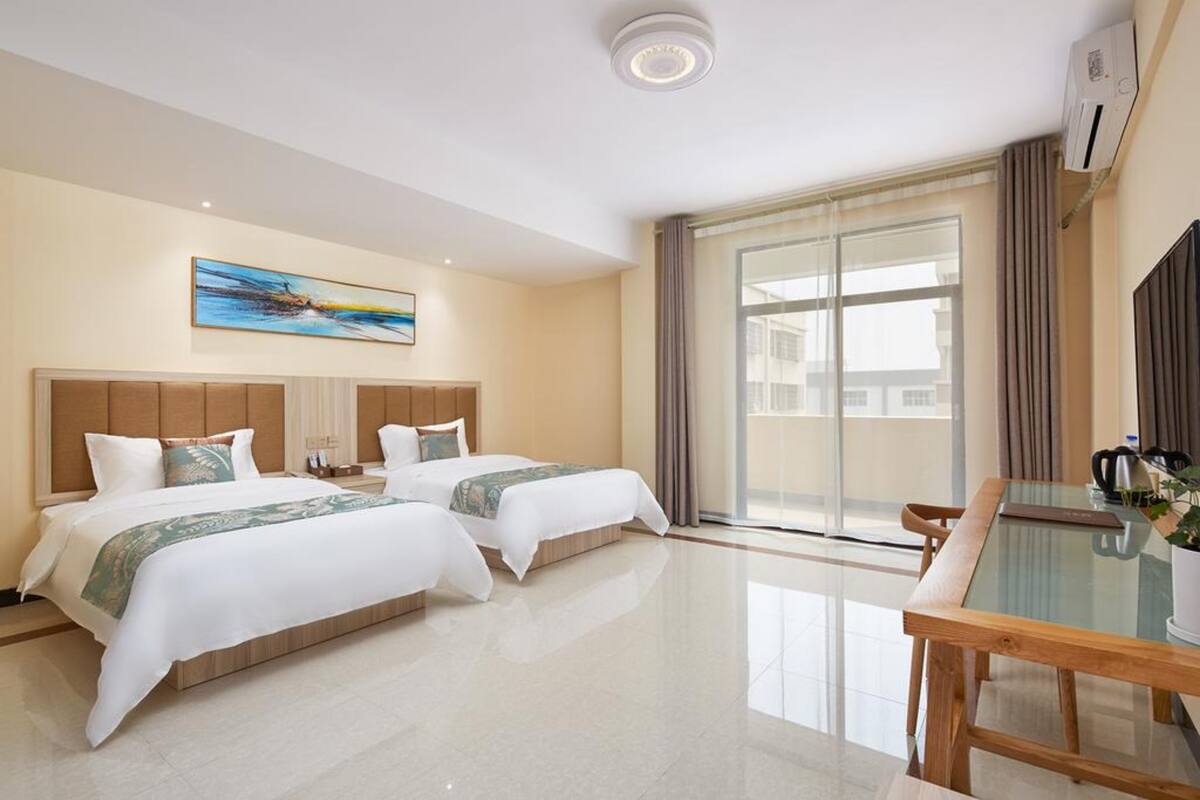 Camera d'albergo con due letti, un tavolo in vetro, una grande finestra con tende e un quadro appeso al muro.