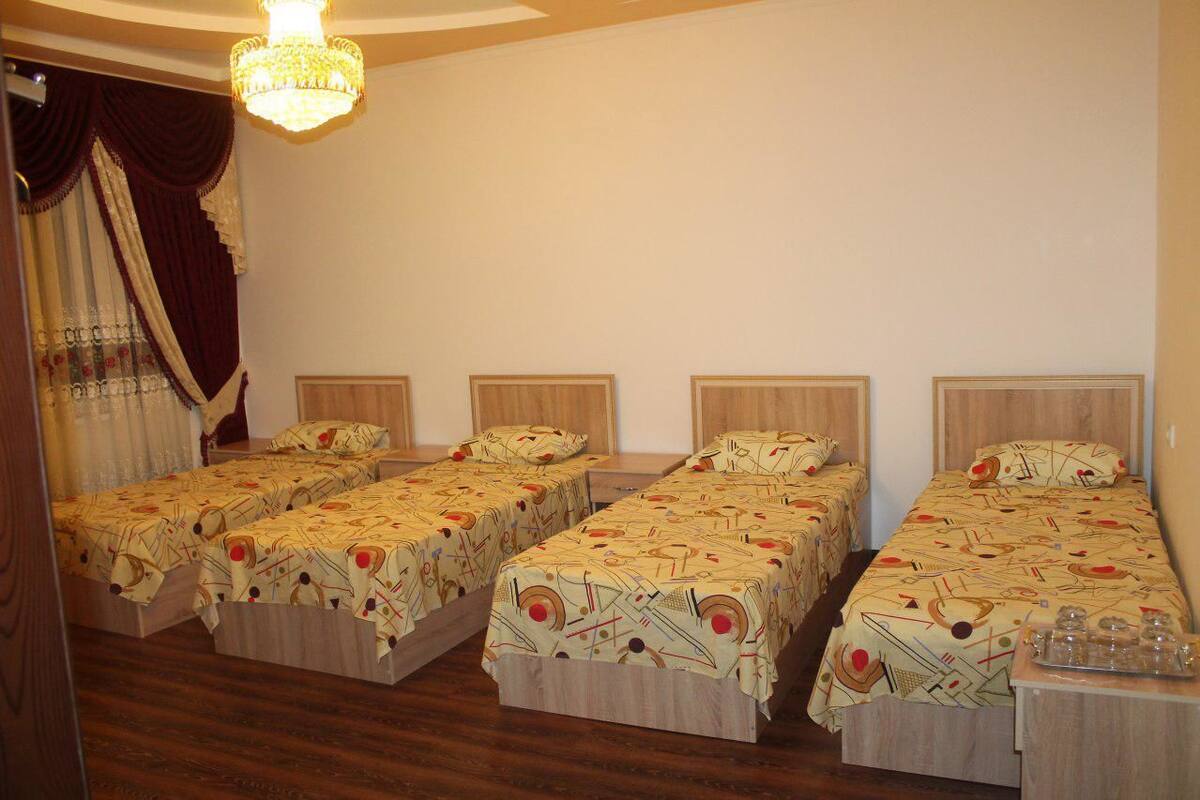 A hotel room with four single beds, a chandelier, wooden headboards, and a wooden floor.