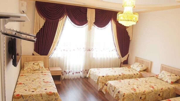 A hotel room with two single beds, a wooden bench, a chandelier, and a large window with curtains.