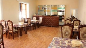 A dining area with wooden tables and chairs, a bar with various bottles, and a large window.