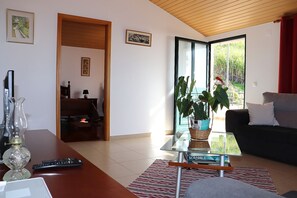 Un salon moderne avec un canapé, une table basse sur laquelle sont posés des livres, une lampe, et une vue sur un balcon, visible à travers une porte vitrée.