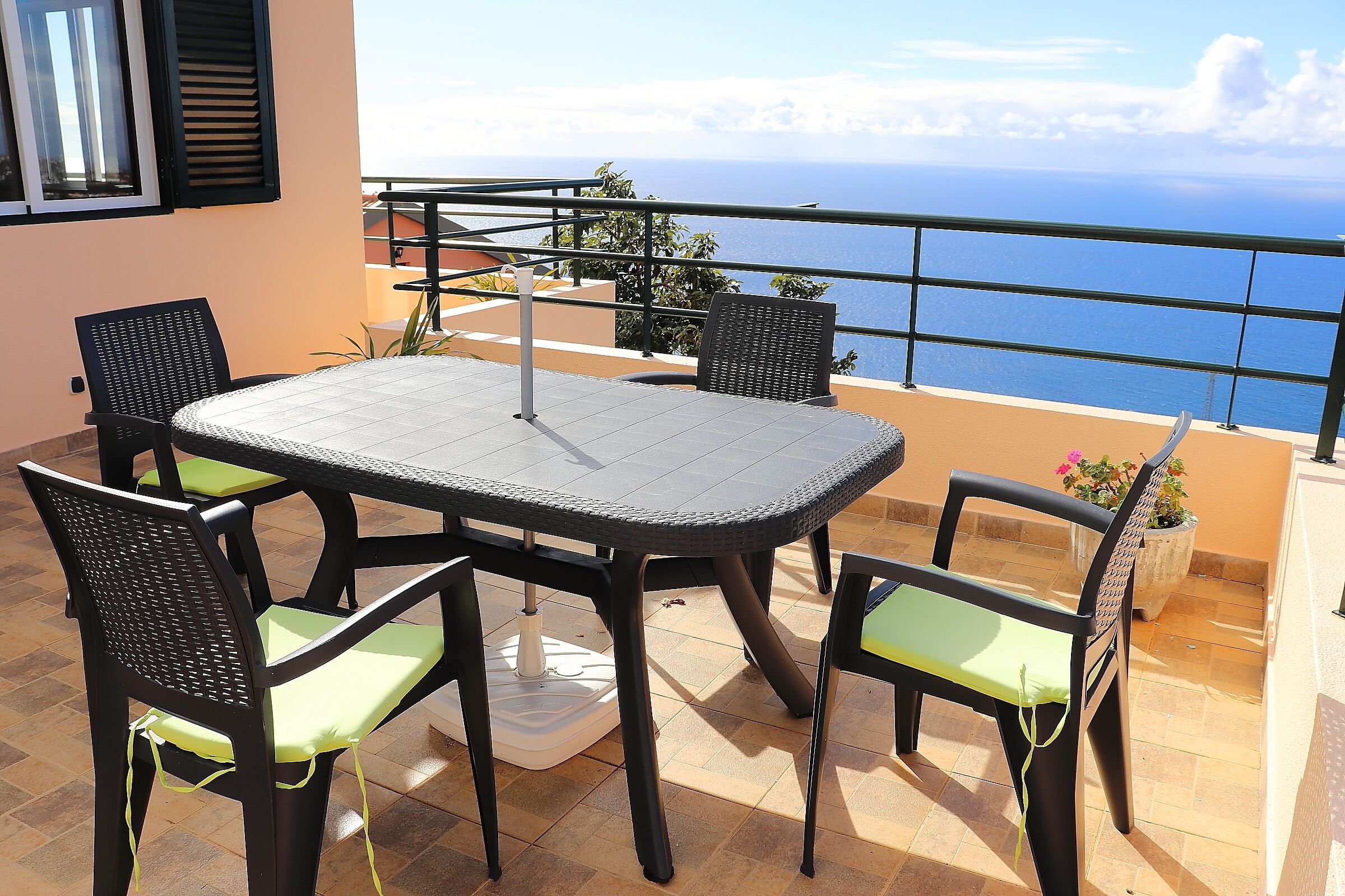 A balcony with a table and chairs, overlooking the sea.