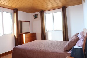 Une chambre à coucher avec un lit, une commode en bois et une fenêtre avec des rideaux.