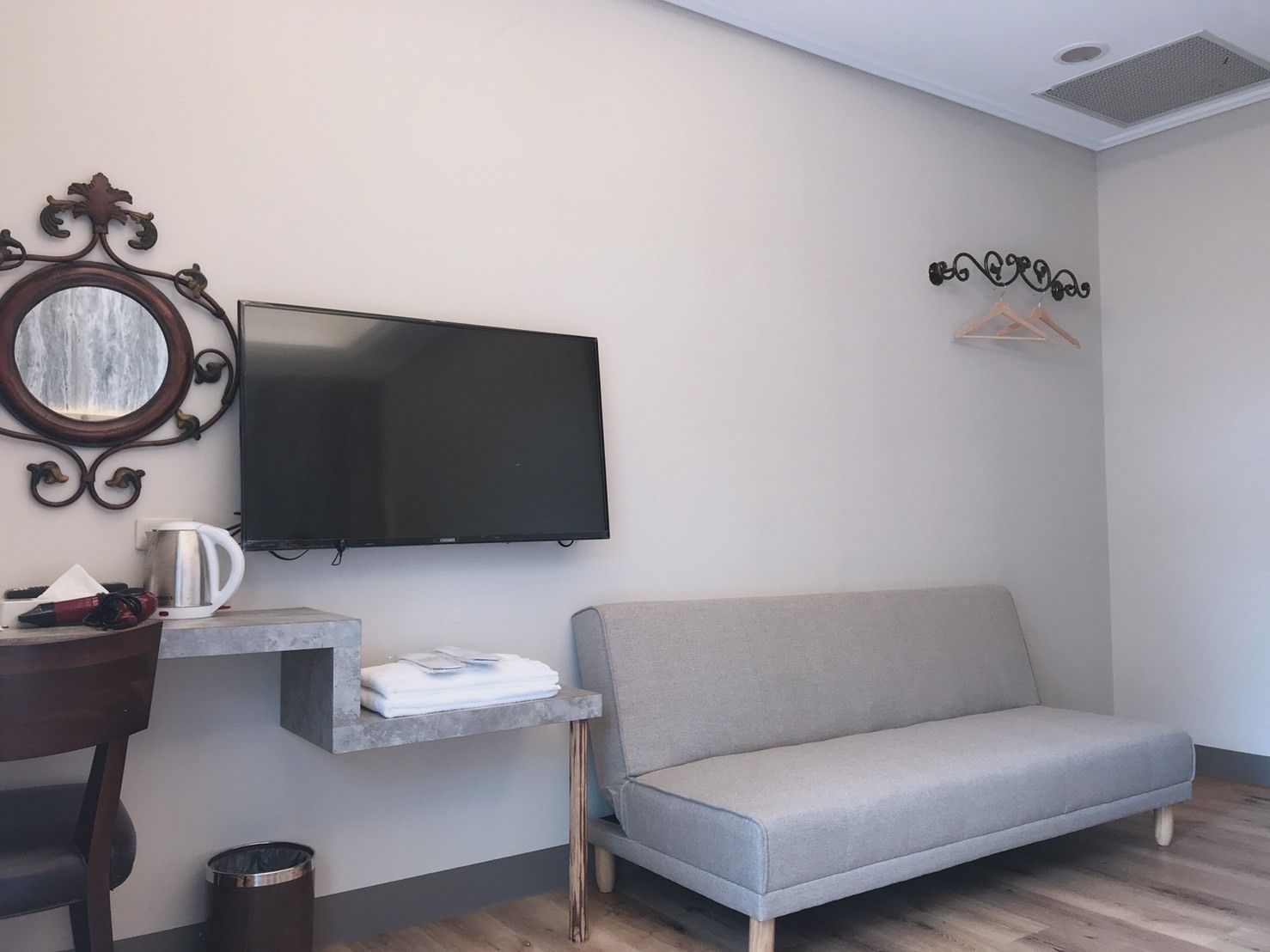 A modern hotel room with a flat-screen TV, a sofa, a small table with a kettle, and a trash bin.