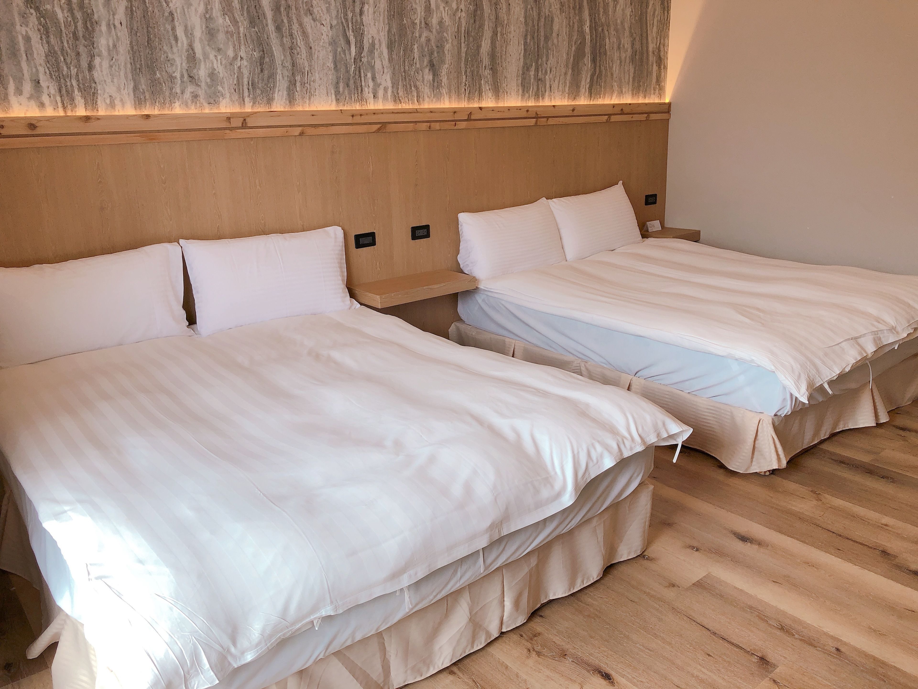 Deux lits simples avec du linge de lit blanc dans une chambre dotée d’un plancher en bois et d’un mur à texture particulière.