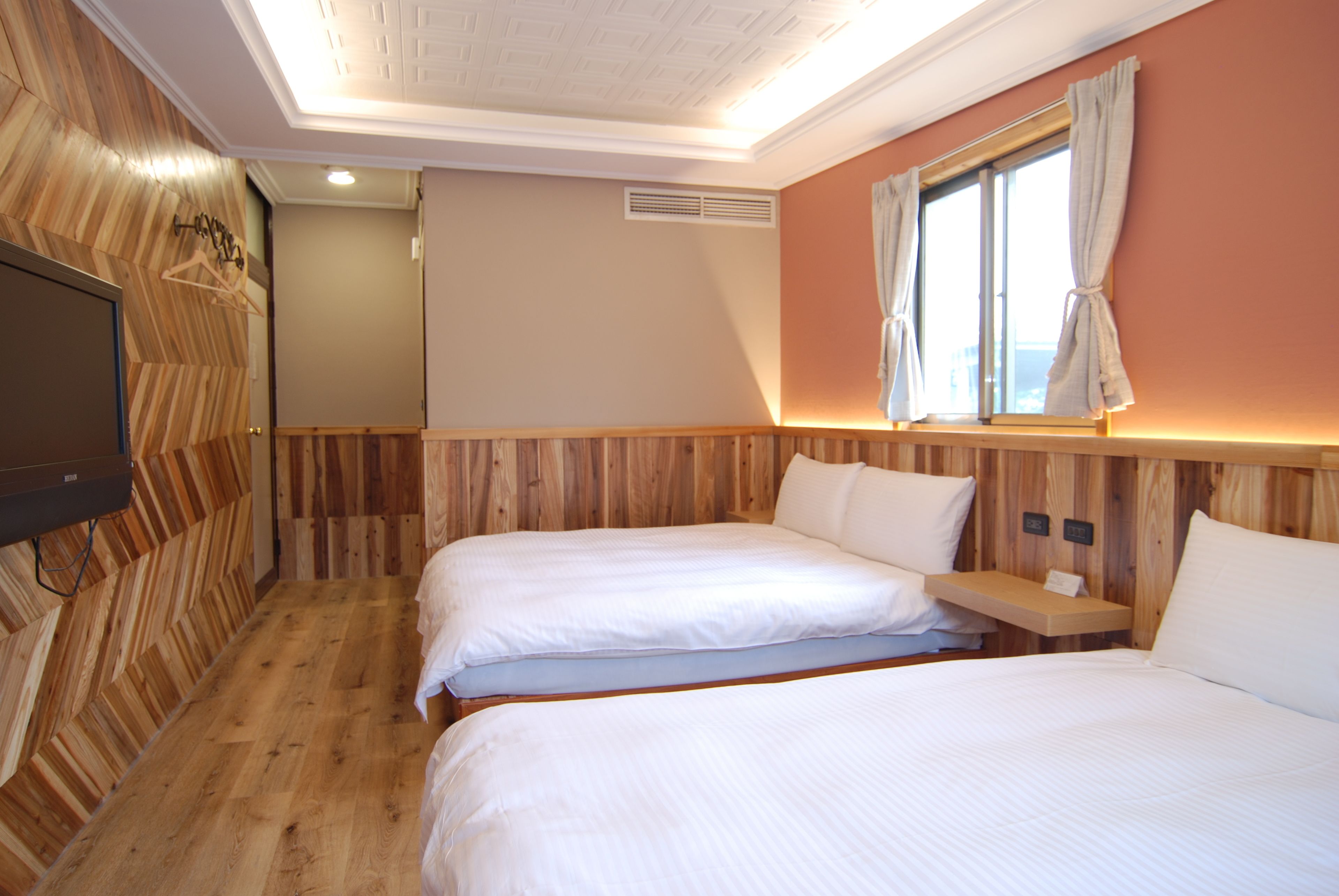 A hotel room with two beds, wooden paneling, a TV, and a window with curtains.