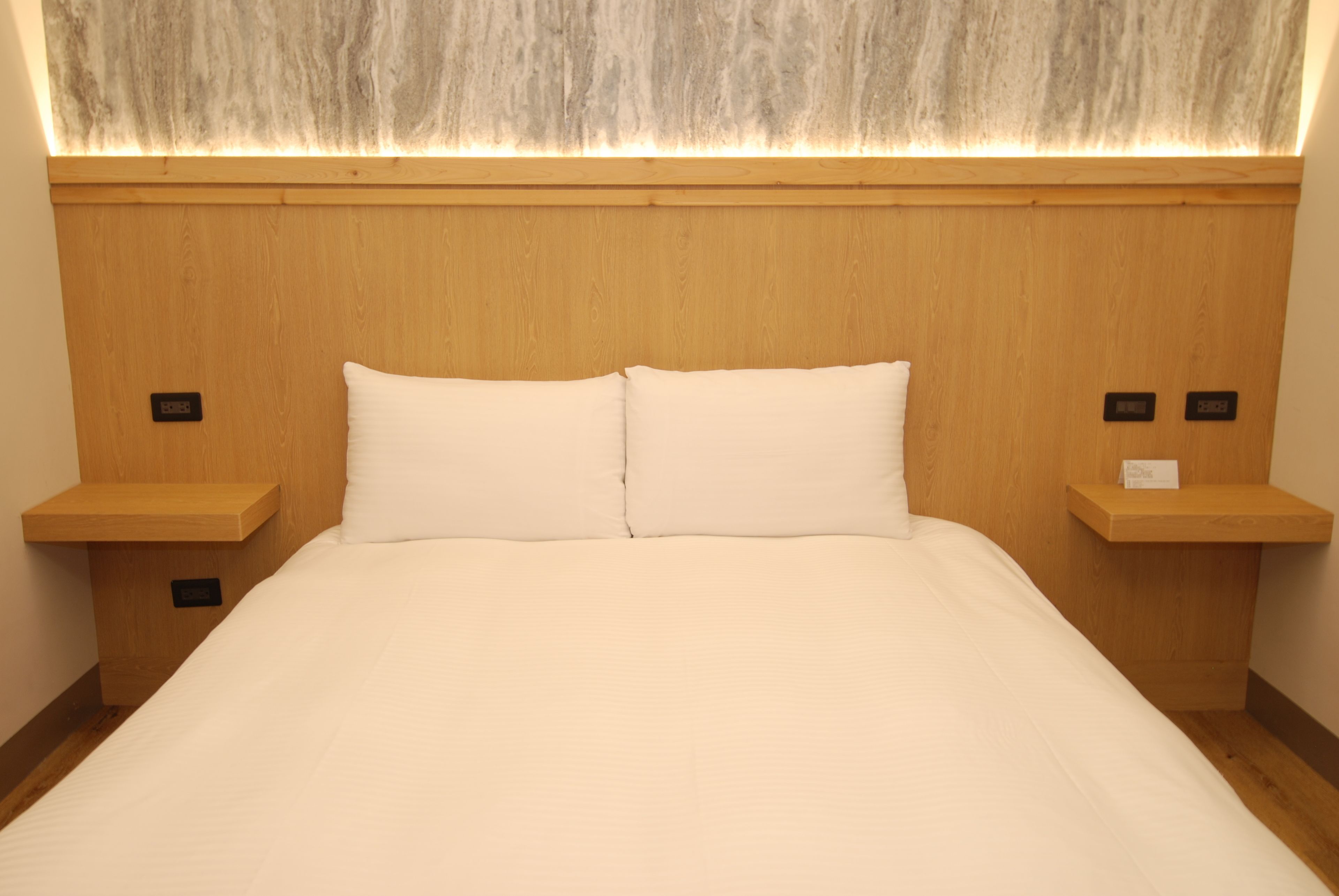 A hotel room with a wooden headboard, two bedside tables, and a large bed with white bedding.