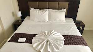 A neatly made bed with white linens, a brown headboard, and a decorative towel centerpiece. - The White House Hotel Samoa (Apia)