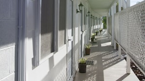 A covered corridor with white walls, doors, and windows, lined with potted plants and black mats. - The White House Hotel Samoa (Apia)