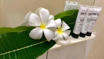 A bathroom shelf with two white flowers and three tubes of soap labeled 'SOAP CO'.
