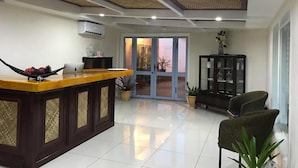 A modern interior with a wooden reception desk, a glass cabinet, and a seating area with chairs. - The White House Hotel Samoa (Apia)