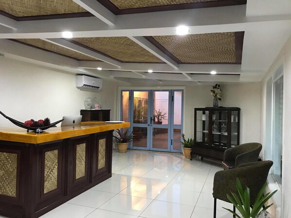 A modern interior with a wooden reception desk, a glass cabinet, and a seating area with chairs.