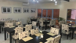 A dining area with multiple tables and chairs, air conditioning units, and framed pictures on the walls. - The White House Hotel Samoa (Apia)