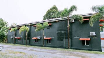A building with multiple air conditioning units, windows with awnings, and a variety of vegetation including palm trees.