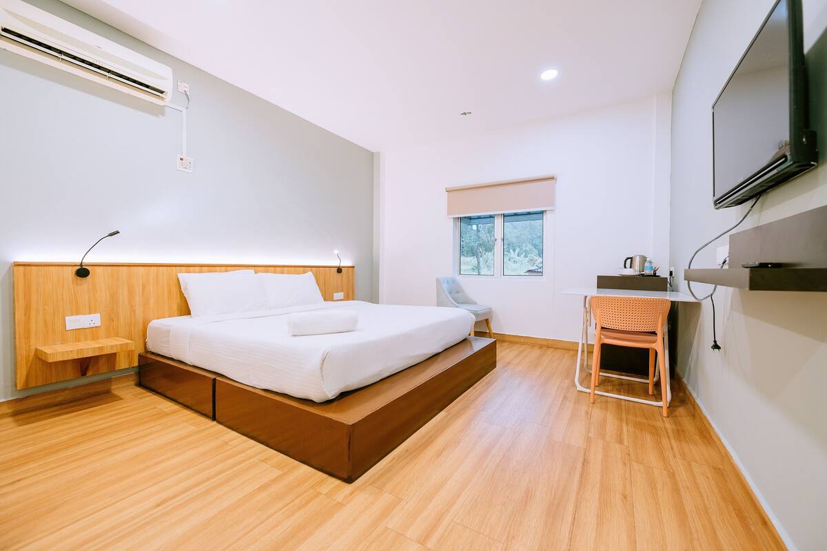 A modern bedroom with a wooden bed, a small desk, and a TV mounted on the wall.