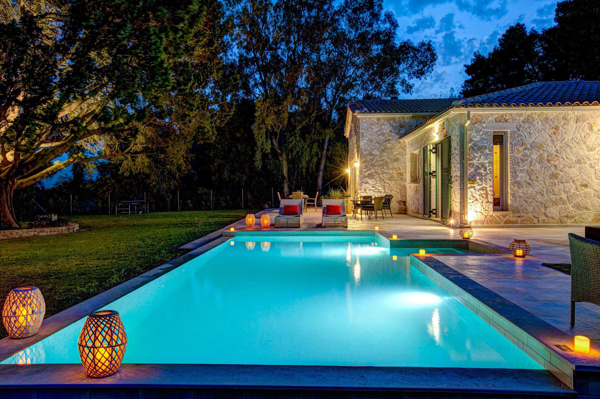 A swimming pool with a stone building in the background, surrounded by trees and outdoor seating.