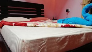 A bed with a white sheet, a red and white patterned blanket, and a blue towel shaped like a swan.