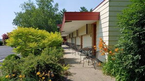 A building with a covered outdoor seating area, a paved walkway, and various plants and flowers. - King Bed - Signature Style (Spring Green)
