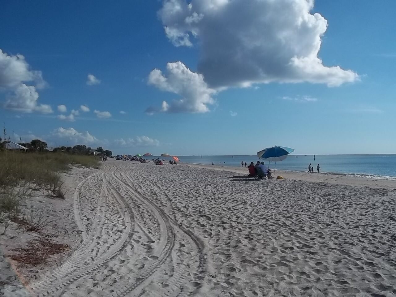 Une plage de sable où l’on peut voir des empreintes menant à l’eau, des parasols et des gens qui profitent de la plage.
