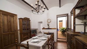 Comedor con una mesa de madera dispuesta para seis personas, rodeada de sillas de madera. Un candelabro cuelga del techo y un aparador se encuentra a la izquierda.