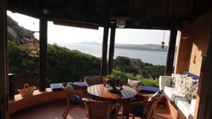 Un espace extérieur aménagé, abrité et doté de sièges, offrant une vue sur la mer, avec des meubles en osier et une table agrémentée d'un vase de fleurs.