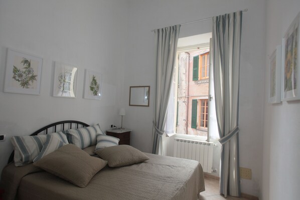 A bedroom with a bed, a nightstand, a window with curtains, and wall art.