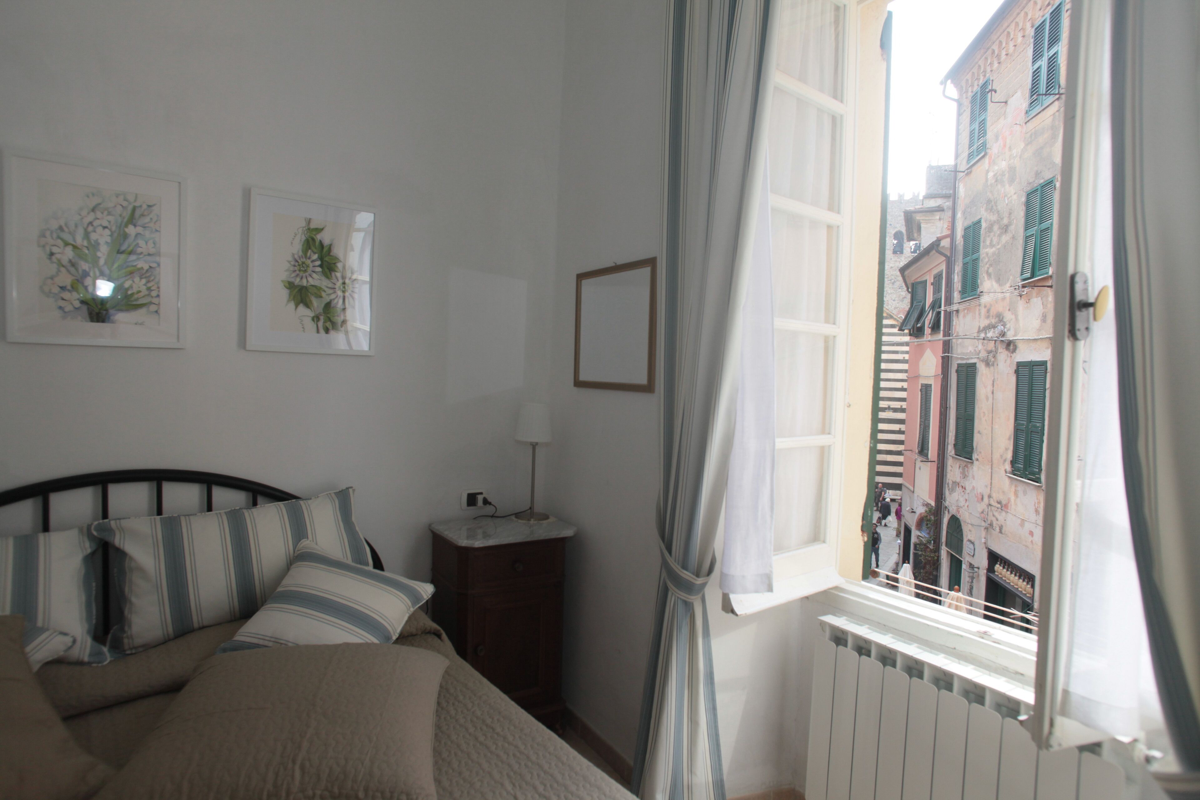 Une chambre à coucher avec un lit, une table de chevet, une fenêtre avec des rideaux et deux tableaux encadrés accrochés au mur.