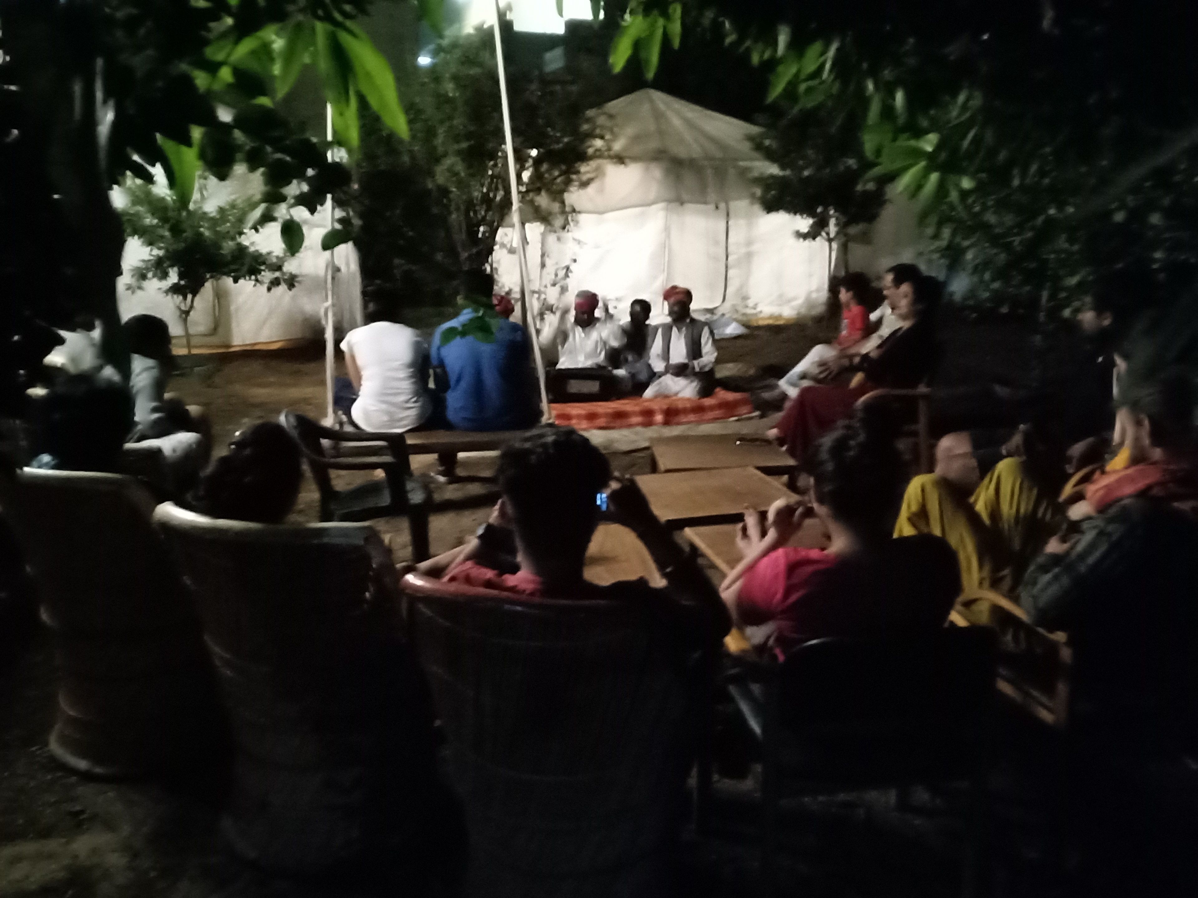 Un grup de persones assegudes a l'exterior d'una tenda, amb algunes persones dempeus.