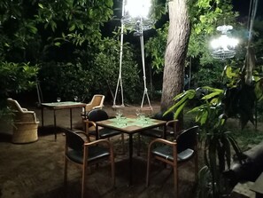 An outdoor dining area with a table and chairs, surrounded by greenery and a hanging light fixture. - Nature Trail Camps & Homestay (Jodhpur)