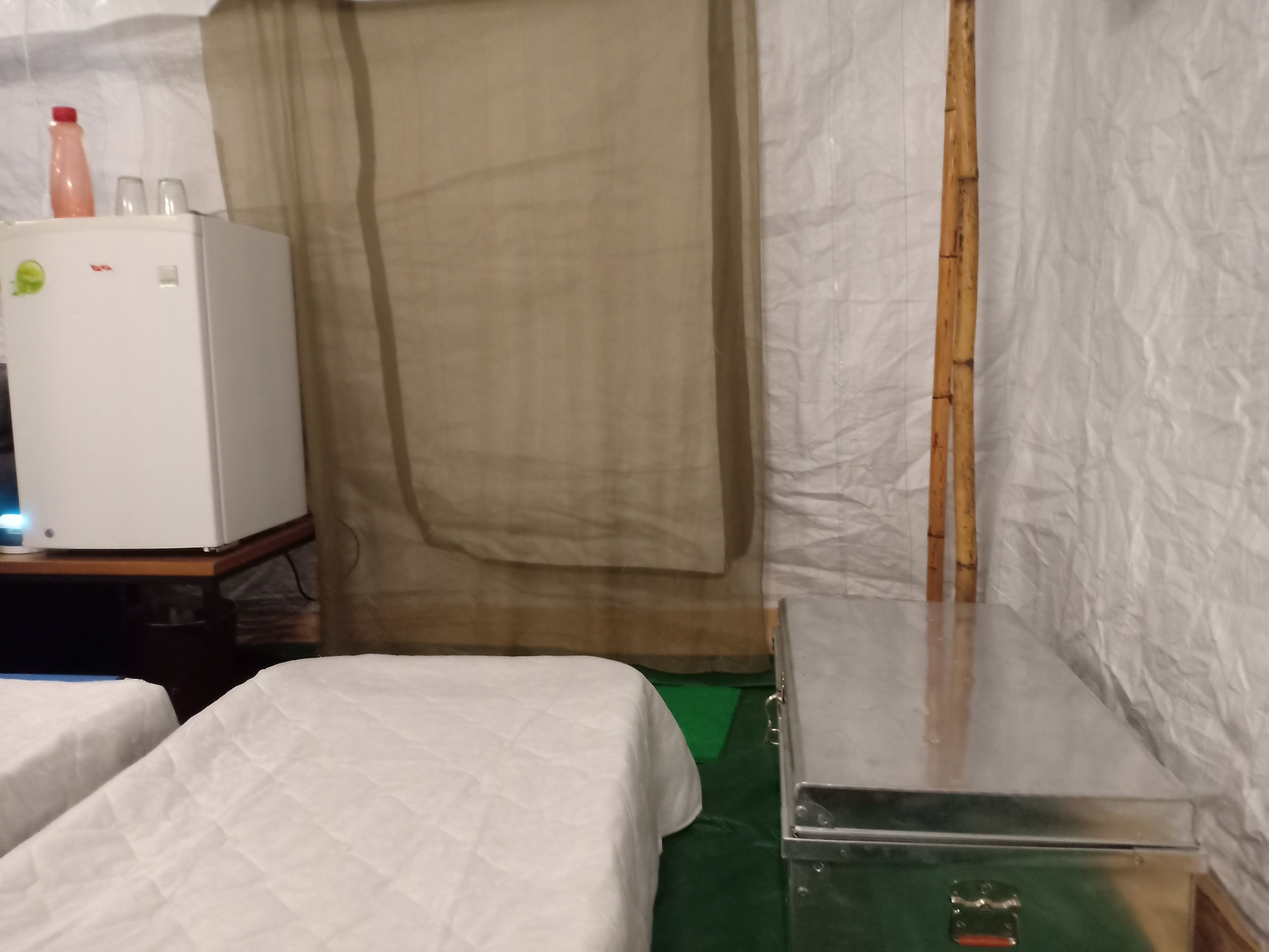 A room with two beds, a small table, a refrigerator, and a curtain.