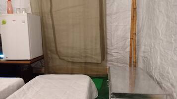 A room with two beds, a small table, a refrigerator, and a curtain.