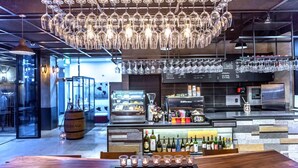 Eine moderne Bar mit einer hängenden Glaskandelaber-Leuchte, einer Auswahl an Weinflaschen und einer Bar, ausgestattet mit verschiedenen Bartools.