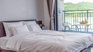 Ein Hotelzimmer mit Bett, Nachttisch, einem Fenster mit Vorhängen und einem Balkon mit Tisch und Stühlen.